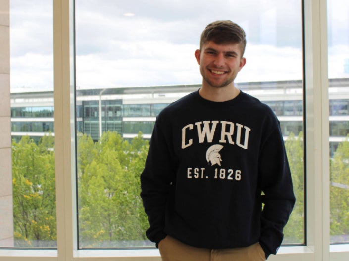Jacob Hoffa stands in front of a window in front of Samson Pavilion wearing a CWRU sweatshirt.