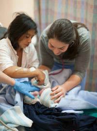 Picture of Brittany Krotzer checking on a patient and their newborn infant in the hospital.