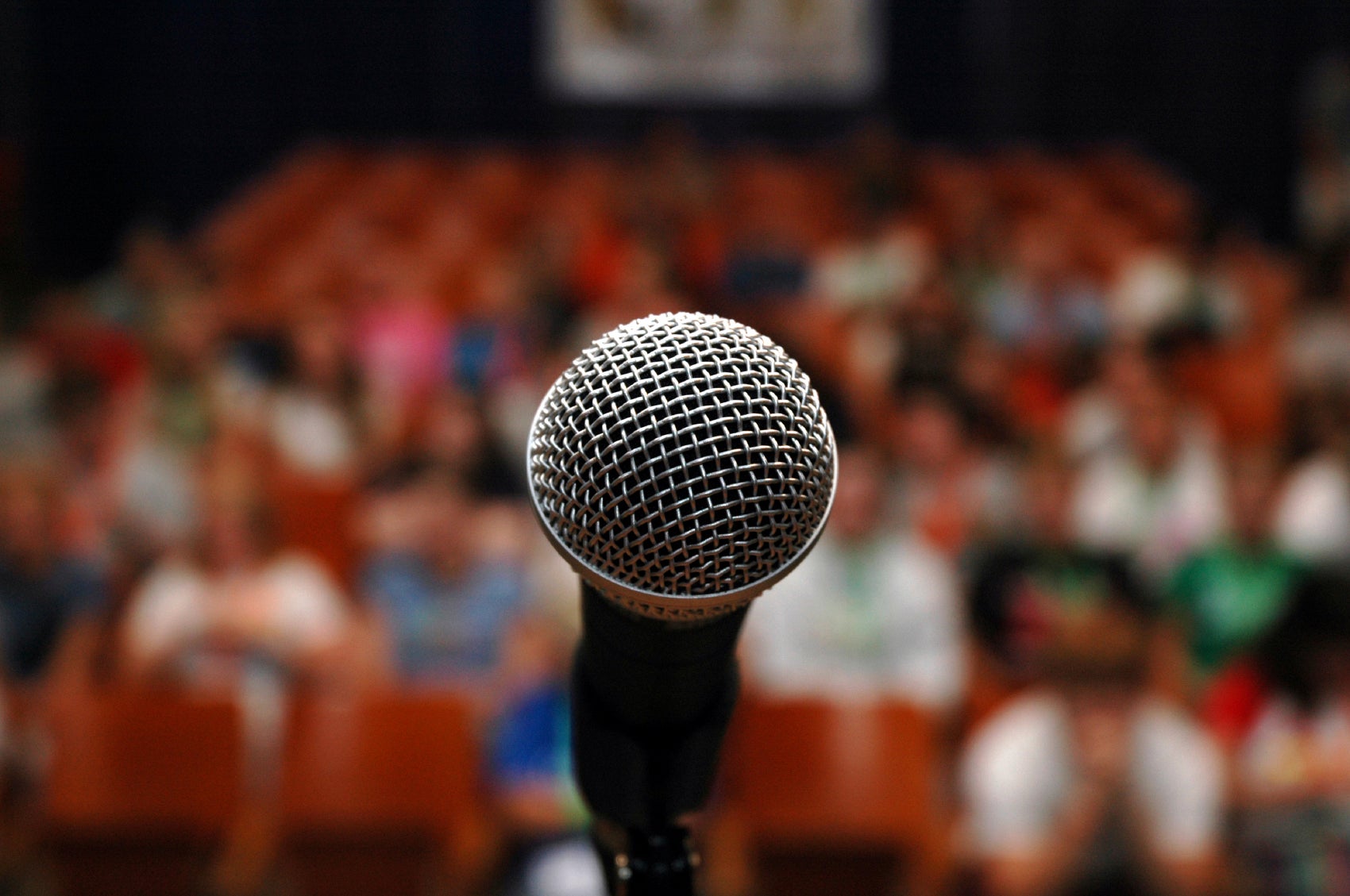 Stock image of a closeup on a microphone with an audience in the background.