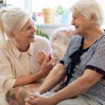 A woman with gray hair cares for an elderly woman at right