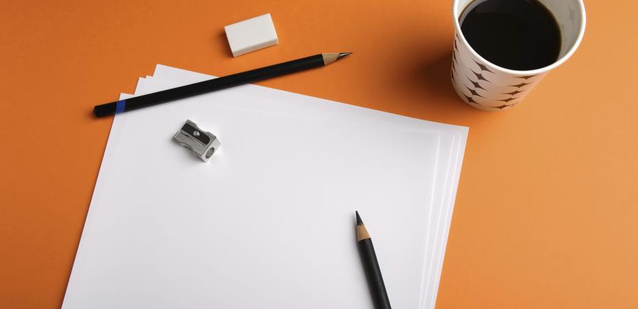Stock image of a cup of coffee next to sheets of blank paper, two pencils, and a tiny pencil sharpener.
