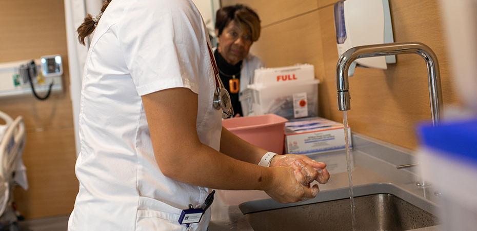 A nursing student practices hand washing techniques as their professor looks on.