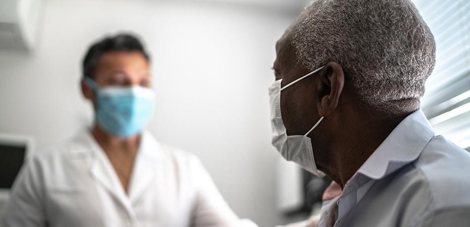 Male patient and healthcare provider during an appointment. Both individuals are wearing face masks.