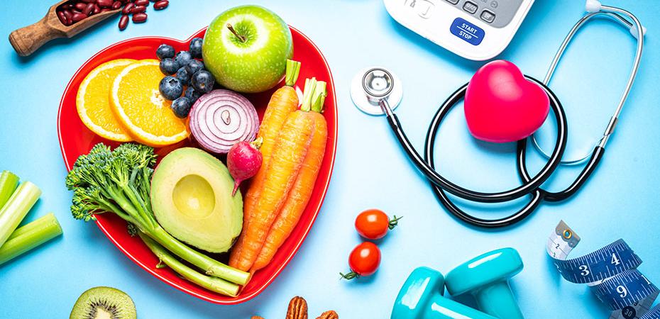 Healthy foods, a scale, weights and a stethoscope laid out on a blue background.