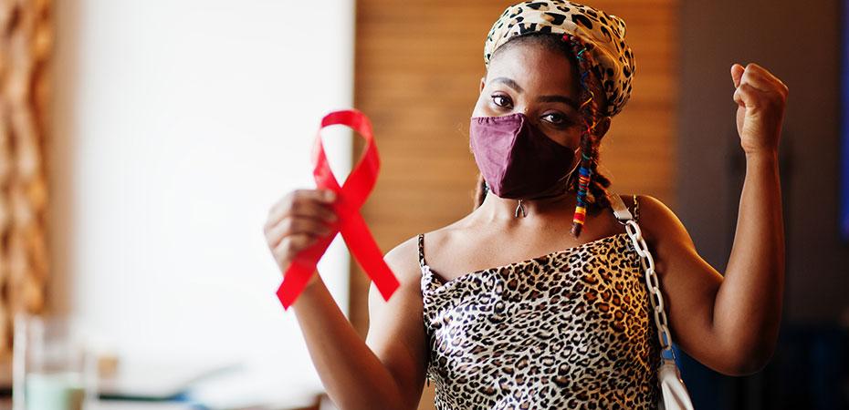 Woman wearing a face mask and holding a red HIV awareness ribbon with her arms raised triumphantly.