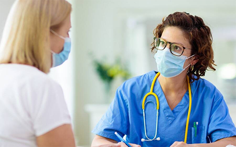 Primary care nurse talking to a patient. Both are wearing face masks.