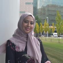 Heba AlDossary in headscarf smiling and leaning against column