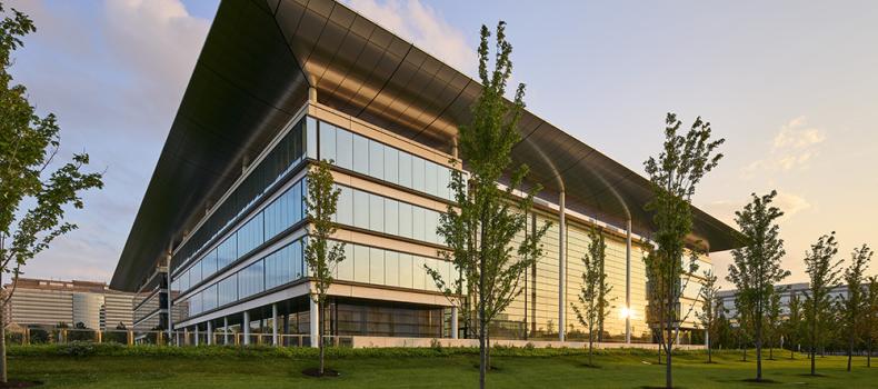 The HEC in sunset, light reflecting off glass windows with green trees in foreground