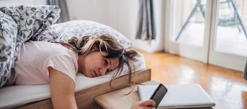 A woman lying in bed reaches for her phone to turn off an alarm