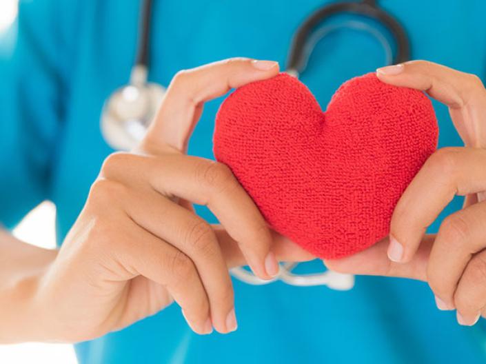 Person wearing blue scrubs and stethoscope holding a red heart.