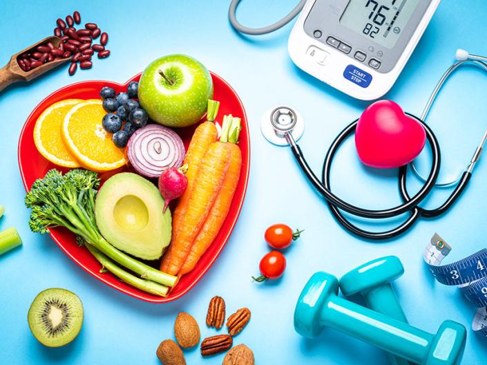 Healthy foods, a scale, weights and a stethoscope laid out on a blue background.