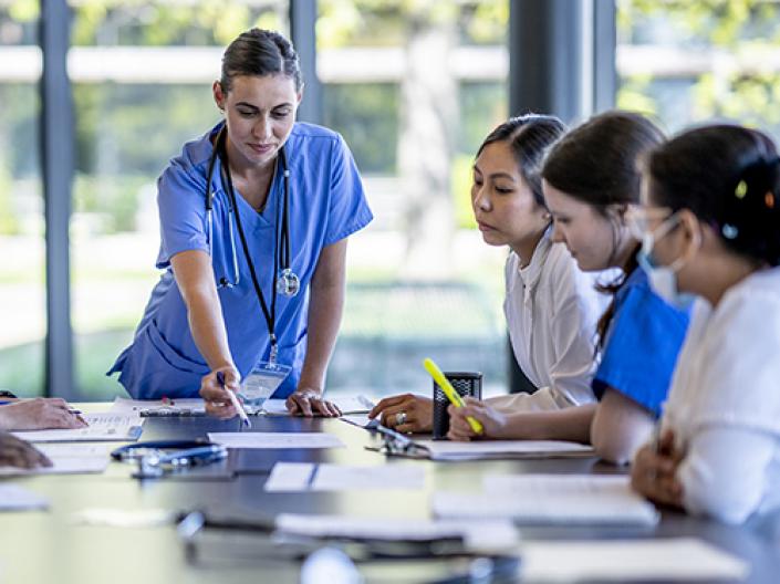 Nurse leader at a table pointing to something while other nurses look on