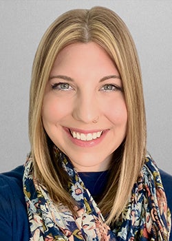 Headshot of smiling blonde woman in blue shirt and floral scarf