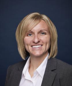 Portrait of a smiling woman with short blonde hair wearing a white blouse and gray blazer