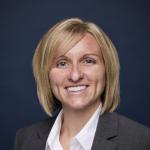 Portrait of a smiling woman with short blonde hair wearing a white blouse and gray blazer