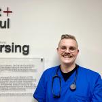Young man in blue scrubs smiles at nursing school