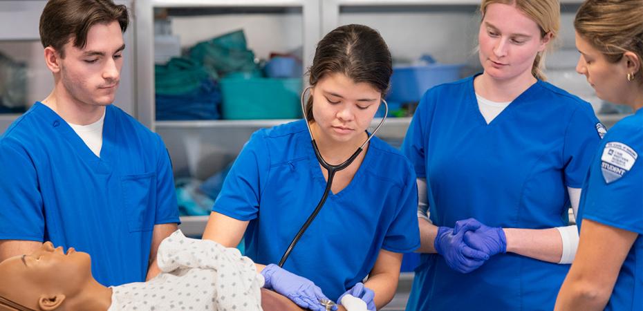 Four nursing students from Case Western Reserve University practice clinical skills on a medical mannequin in a simulation lab.
