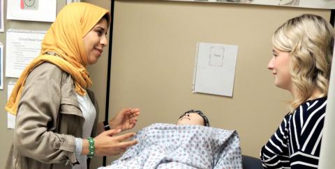 Picture of two women discussing techniques over a dummy patient. 