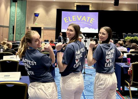 A trio of female nurses point to a saying on the back of their t-shirts