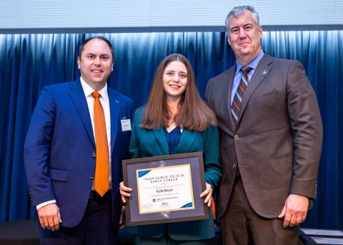 Kylie Meyer, center, holding her Innovator of the Year award, with two men on either side of her.