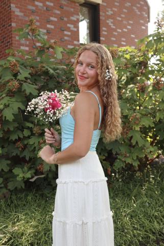 A curly haired blonde girl looking over shoulder while holding flowers