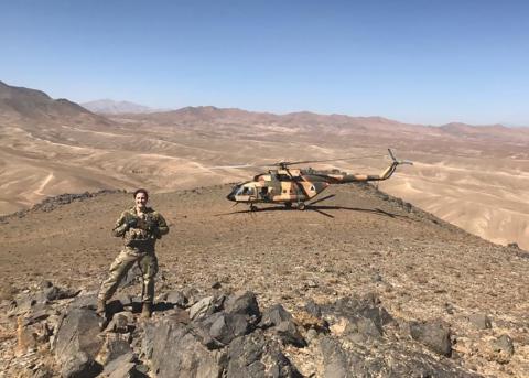 A woman in military uniform stands in the desert next to a helicopter