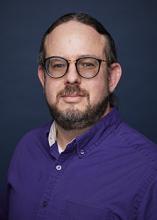 A headshot portrait of Matt Plow wearing purple shirt and glasses