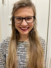 Anna Lloyd, a girl with blonde hair and glasses wearing a gray sweater