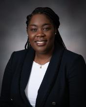 A portrait of a smiling dark-skinned woman wearing a suit