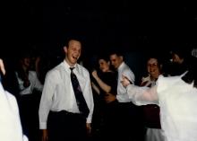 A photo of people partying with a man in white shirt and black tie smiling as he dances