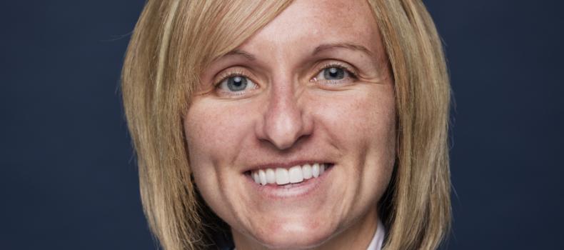 Portrait of a smiling woman with short blonde hair wearing a white blouse and gray blazer