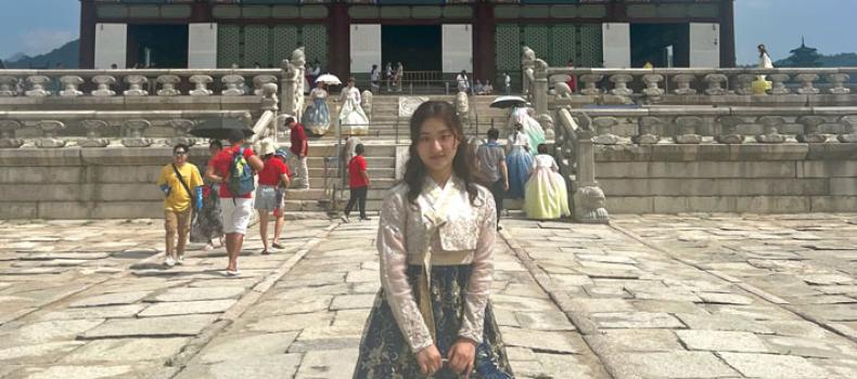 Sohee Kim in traditional Korea clothes stands in front of Gyeongbokgung Palace in South Korea