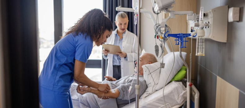 Stock image of a nurse in blue scrubs and nurse in white coat helping a patient in bed