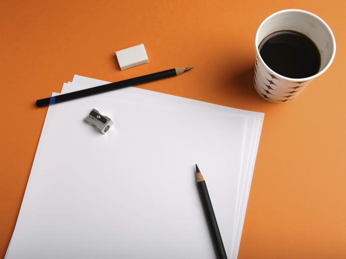 Stock image of a cup of coffee next to sheets of blank paper, two pencils, and a tiny pencil sharpener.
