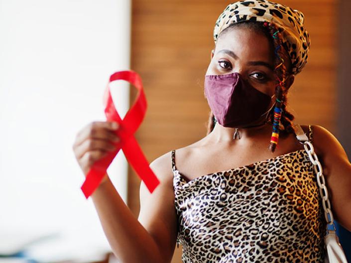 Woman wearing a face mask and holding a red HIV awareness ribbon with her arms raised triumphantly.