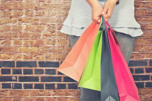 Women leaning against brick wall holding different color shopping bags