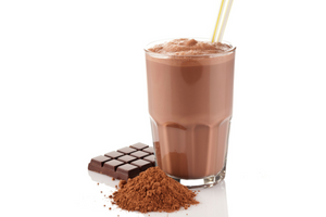 chocolate shake in glass cup with yellow straw and cocoa powder and chocolate bars beside it