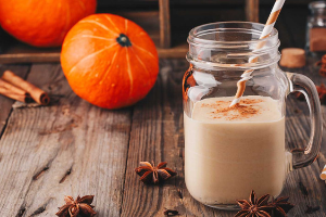 pumkin chai shake with orange and white striped straw. pumpkins, cinnamon sticks, and star anise scattered on a wooden table