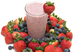 A smoothie surrounded by strawberries and blueberries
