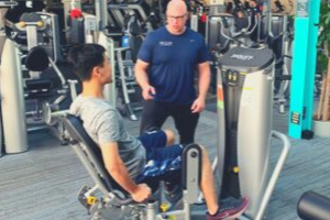 Man in blue shirt personal training client on a leg machine weight