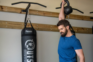 Man holding kettlebell overhead in front of a heavy bag