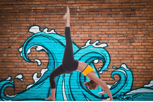 Woman back bend yoga pose with foot in air in front of wall with graffiti