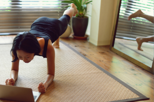 Woman in plank pose on floor of bedroom looking at computer