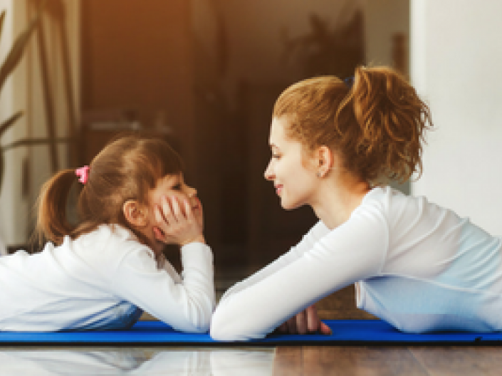 Mother and daughter lying on floor on yoga mats looking at each other with chin in hands