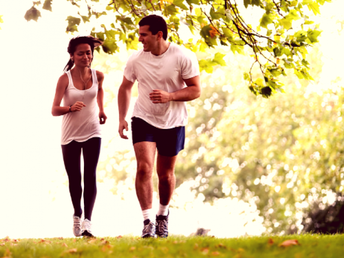 man and woman walking outside on the grass, trees in background