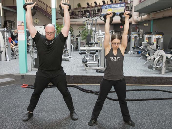 Man and woman lifting kettlebells overhead