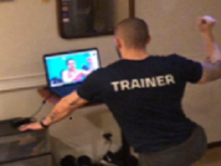 Man with trainer on the back of shirt looking at someone on computer screen
