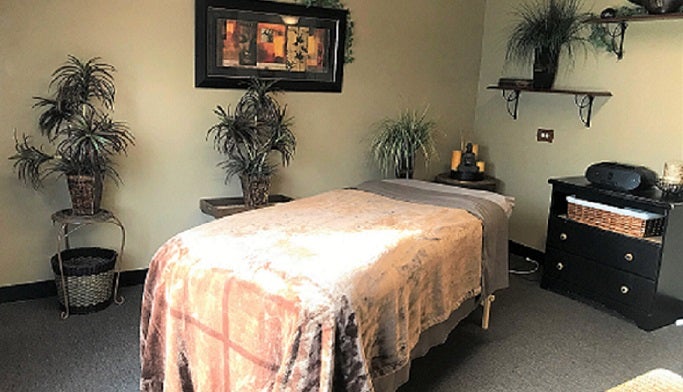 Massage room with bed in middle and plants and pictures along wall