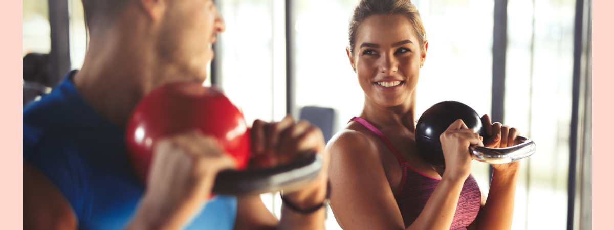 man and woman holding kettlebells smiling looking at each other