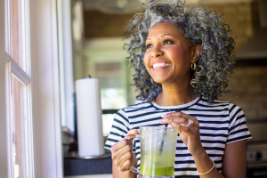 Woman with curly hair, striped shirt, smiling and holding a green smoothie
